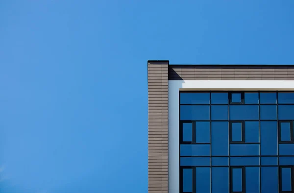 The edge of the facade of a modern building with glass mirrored windows against the blue sky. Place for text