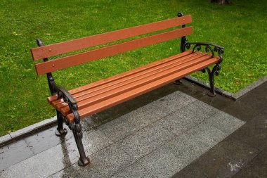 An empty bench in the park on a rainy day. Modern wooden bench with forged metal Close-up