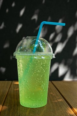 A plastic glass with a straw and a drink stands on a table outside. Outdoor bar on a sunny day