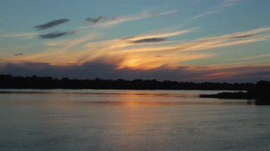 Sirus bulutlarıyla nehrin üzerinde gün batımı. Bulutlar gökyüzünde soldan sağa doğru uçar. Dinyeper Nehri 'nin suyu sağdan sola akar. Ufukta bir orman var. Zaman Uygulaması