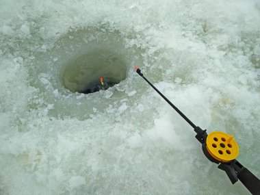 Balıkçı oltası ve şamandırayla buz balıkçılığı. Buzdaki deliğe yakın çekim.