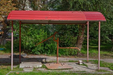 Bahçedeki bir gölgeliğin altında elle su pompası. İçme suyu tedarik etmek için bir sütuna yakın çekim. Arka planda ağaçlar ve yeşil çimenler