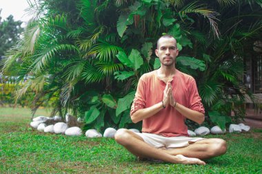 Nilüfer pozisyonunda oturan bir adam ellerini sımsıkı tutuyor. 