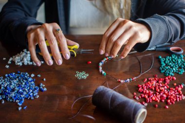 Hands of female person making handmade necklace with tweezers an