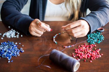 Female hands making handmade necklace with blue, red, green and 