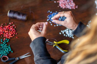 Hands of a female person making a handmade necklace seen from be