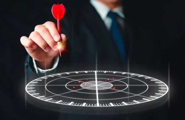 Businessman hand holding red dart put to centre of red target board. Concept Setting life goals, Business planning That will make it successful in the future, Investment.