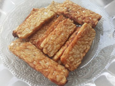 Slices of cooked tempe that have been fried are served on a patterned glass plate. Tempe is a traditional Indonesian food.
