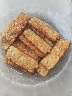 Slices of cooked tempe that have been fried are served on a patterned glass plate. Tempe is a traditional Indonesian food.