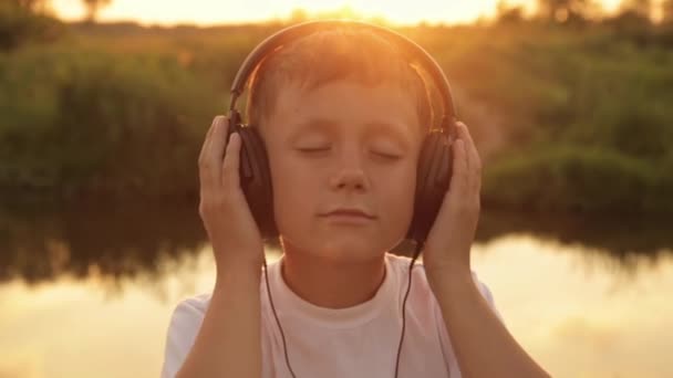 El muchacho que escucha la música en los auriculares por la naturaleza, el verano, la puesta del sol — Vídeos de Stock