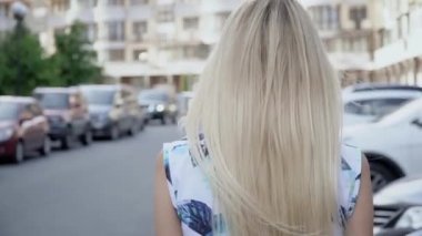 Otoparkta poz veren yazlık takım elbiseli bir sarışın. Kamera kabloları. Kadınlar yürür