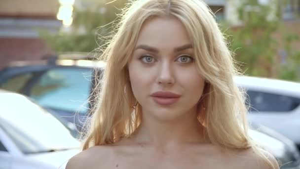 Portret van een blonde met volle lippen en blauwe ogen op een achtergrond van parkeren — Stockvideo