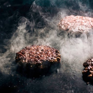Tavada kızarmış hamburger pirzolası. Yağlı ve yağlı bir hamburgerden bolca beyaz duman çıkıyor..