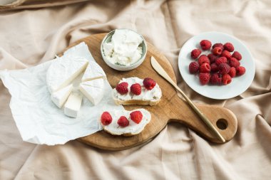 Estetik kahvaltı camembert, krem peynirli bruschetta ve ahududu ahşap tahtada.