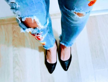 Yırtık kot pantolon ve yüksek topuklu ayakkabı giyen bir kadın. Modern ve şık..