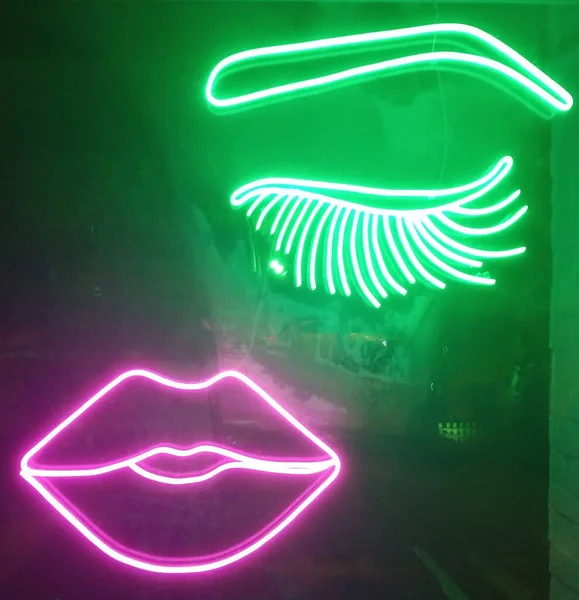 Pink lip neon, green eyebrow neon.  Neon with eyebrow and lip light on glass. Attractive for cosmetic and beauty sector.