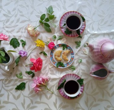 İki fincan kahve, pasta ve çaydanlık renkli çiçeklerle dolu..