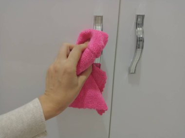 Cabinet handles are cleaned with a pink cloth.