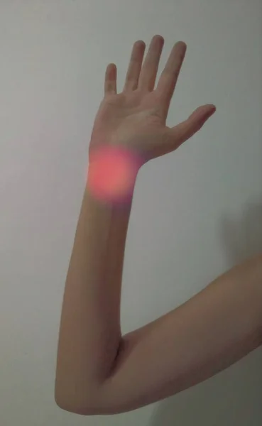 Female arm. There is a red round light on the wrist. A good example for the healthcare industry. Body part.