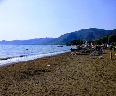 İnsanlar kumsalda güneşleniyor. Bazıları denizde yüzüyor. Hisaronu-Marmaris
