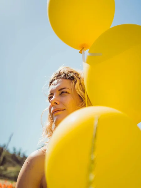 vertical portrait of smiling girl holding yellow balloons in a midsummer day