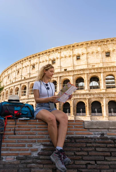 Young woman tourist searches sitting in her map for city attractions on a sunny summer day, digital nomad, vertical shot