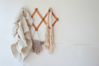 Dekorasyon malzemeleri ahşap bir askıda beyaz bir duvara asılıdır. Makrame, havlular. Kırsal biçim.