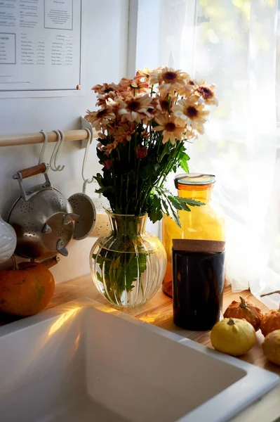 Um buquê de margaridas fica na cozinha perto da pia. luz de uma grande janela. Espaço rústico acolhedor. Imagens De Bancos De Imagens