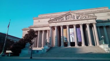Time-lapse of the National Archives Building in Washington, D.C. at sunset, seen from Constitution Avenue NW. Car and tourist foot traffic is seen. The camera pans left to right.