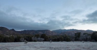 Dawn sunlight illuminates the Chiricahua Mountains as clouds pass by in the Coronado National Forest in Arizona as seen from a meadow in Rucker Canyon on a winter morning. Turtle Mountain is visible.
