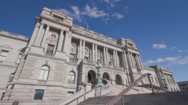 The Library of Congress - Thomas Jefferson Building located at 101 Independence Ave SE in Washington D.C.'s Capitol Hill neighborhood. Static, low-angle wide shot with blue sky and clouds. No people.
