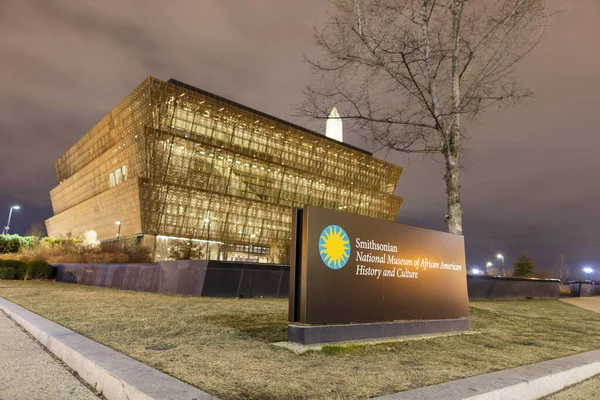 Smithsonian Ulusal Afro-Amerikan Tarihi ve Kültürü Müzesi 'nin bir kış akşamında görülen bir işareti. Arka planda müze ve Washington Anıtı görülüyor. Washington, DC şehir merkezinde yer alıyor..