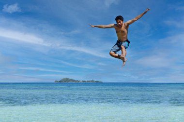 young man jumping in the air at the beach of Raja Ampat. Carefree people vacation time concept image.