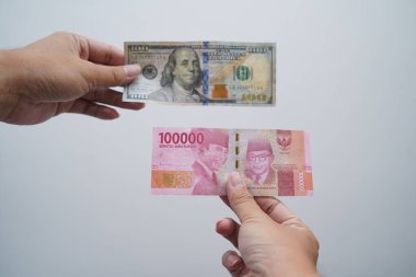 hand holding one hundred thousand rupiah and one hundred dollars isolated on white background