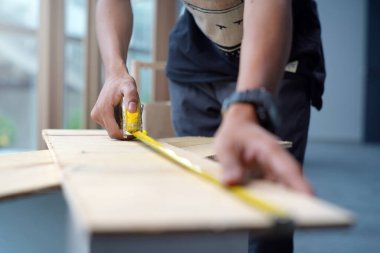 Worker measuring the length of a wooden deck with a tape measure in a workshop. Selective focus photo