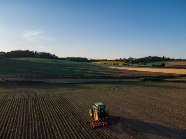 Bir çiftçi yaz günbatımına kadar traktörle tarlayı hasat ediyor.