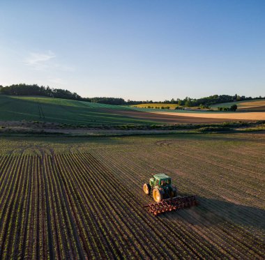 Bir çiftçi yaz günbatımına kadar traktörle tarlayı hasat ediyor.