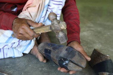 Traditional shoemaker with hammer making handmade shoes for selling. Closeup of Hands of man hammering on leather nailed with a wooden frame called last. 