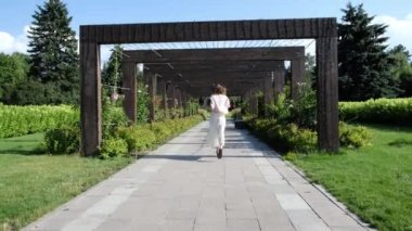 Güzel kız parkta kemerlerin arasından koşar. Yüksek kalite 4k görüntü
