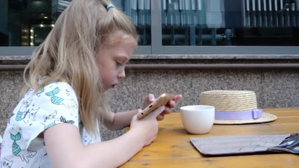 小女孩坐在咖啡店的桌子边 一边看着智能手机 高质量的4K镜头 — 图库视频影像