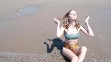 Genç ve güzel bir kadın sahilde oturur ve saçlarına dokunur. Yüksek kalite 4k görüntü