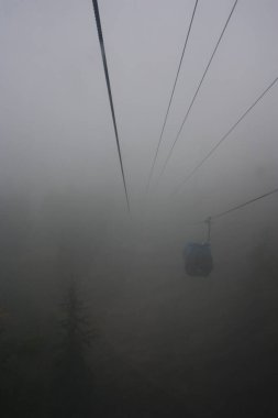 An outside shot of a gondola going through the fog or mist as it travels up the mountain.