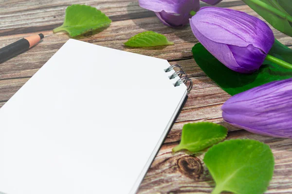 Notepad and pencil with flowers on wooden desk. Copy space. Flat lay.