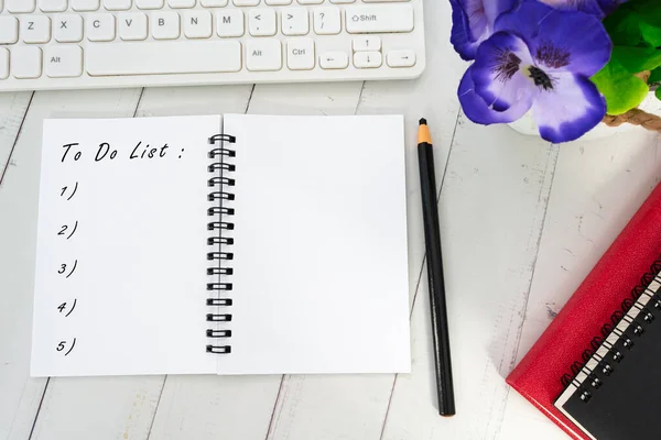 To Do List text on notepad with pencil, computer keyboard, books and potted plant.