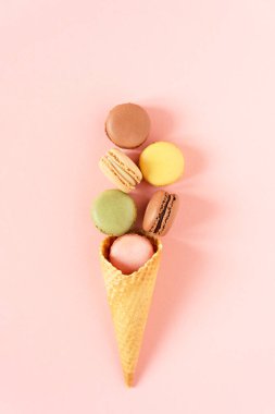 Pembe arka plan manzaralı waffle dondurma külahında çeşitli badem kurabiyeleri. Fransız kurabiyeli kurabiyelerin yaratıcı bileşimi..
