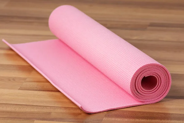 Pink exercise mat on wooden floor. Home workout concept.