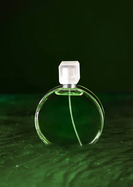 Green bottle of French perfume in green water. Fresh perfume on wavy water.