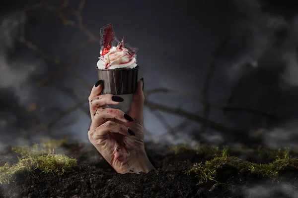 Hand out of grave holding Halloween cupcake. Halloween muffin. Halloween creative food.