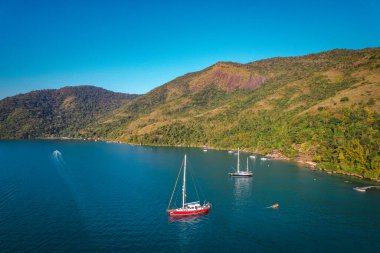 Mavi suyu ve yatları olan, tropikal bir ormanı ve havadan manzarası olan bir göl.