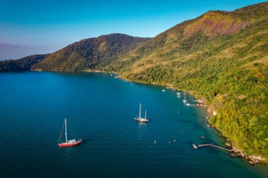 Mavi suyu ve yatları olan, tropikal bir ormanı ve havadan manzarası olan bir göl.